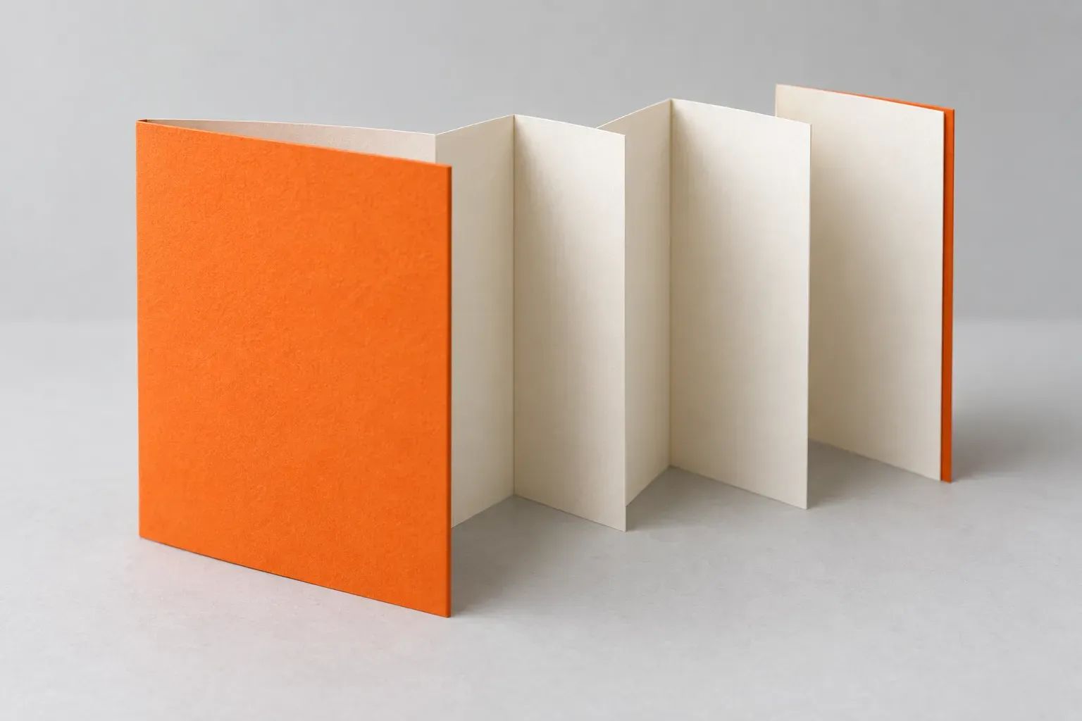 An orange accordion-fold booklet opens to reveal several cream paper panels.