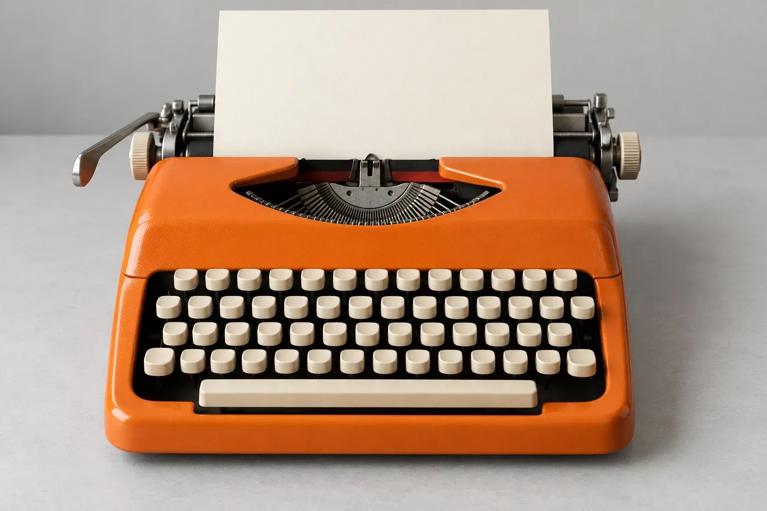 An orange typewriter with cream keys holds a blank sheet on a grey desk.