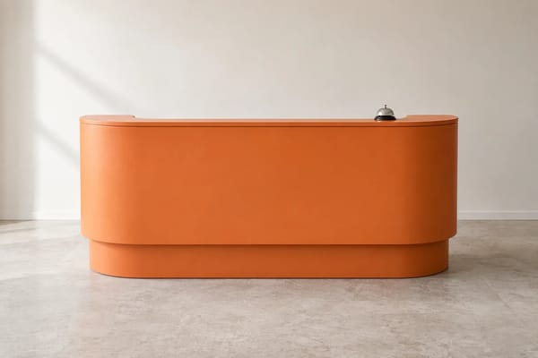 An orange reception desk with a small silver service bell in a calm office.