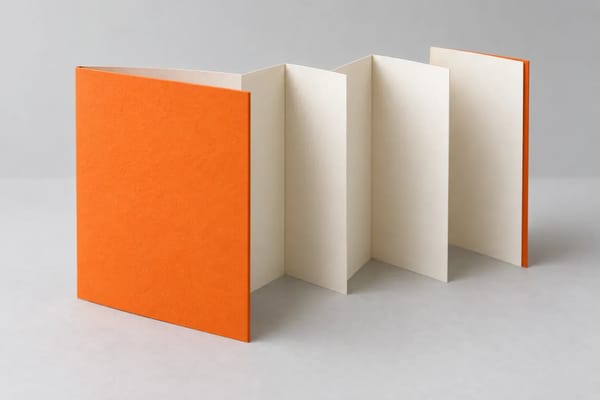 An orange accordion-fold booklet opens to reveal several cream paper panels.