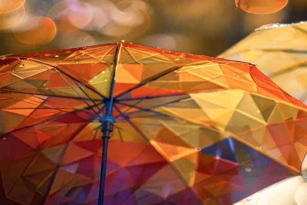 Close-up of an umbrella with faceted orange, yellow and violet glass panels, seen from below against warm blurred lights