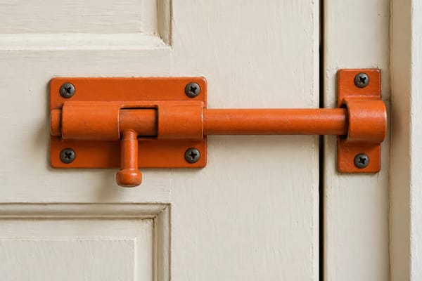 An orange door bolt is fastened across a plain cream wooden door.