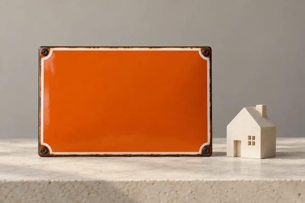 An orange address plaque sits beside a small cream house model on a pale surface.