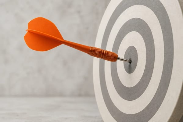An orange dart sits in the centre of a cream circular target.