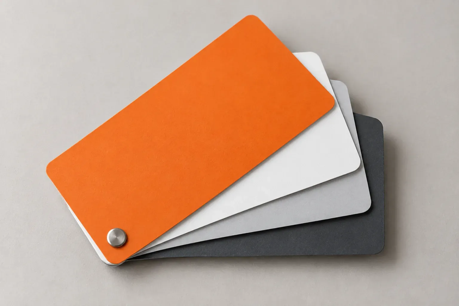 An orange colour swatch fanned over white, grey and charcoal cards on a neutral surface.