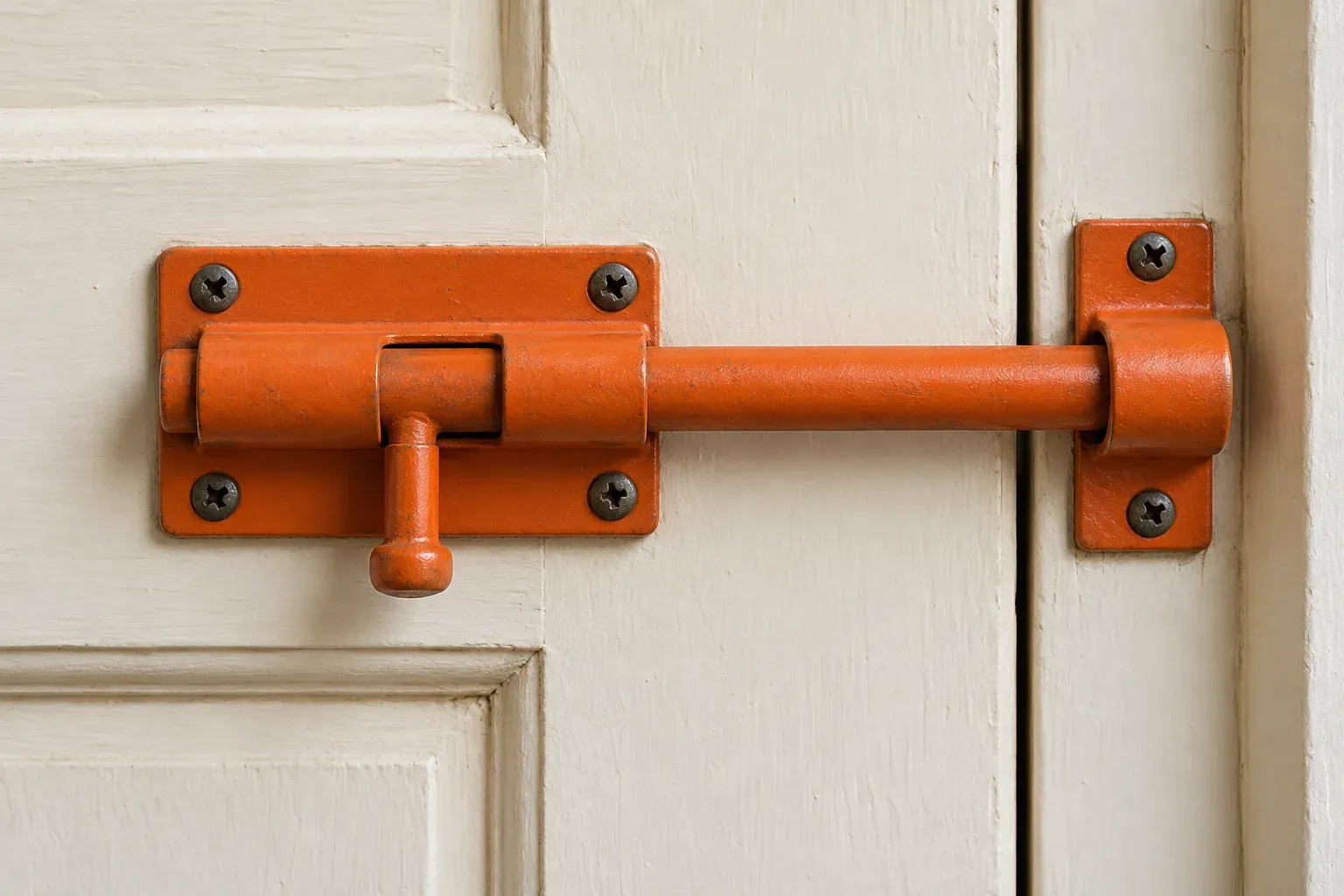An orange door bolt is fastened across a plain cream wooden door.