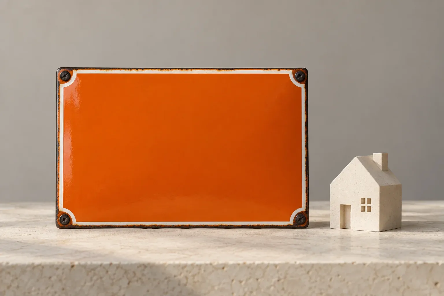 An orange address plaque sits beside a small cream house model on a pale surface.