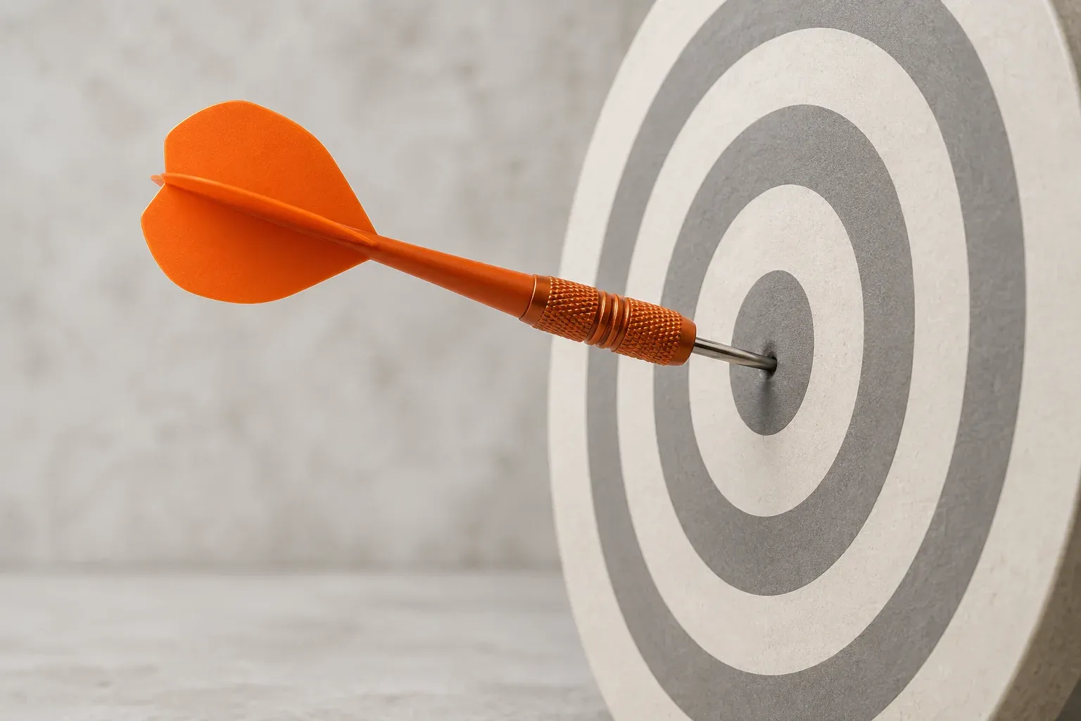 An orange dart sits in the centre of a cream circular target.