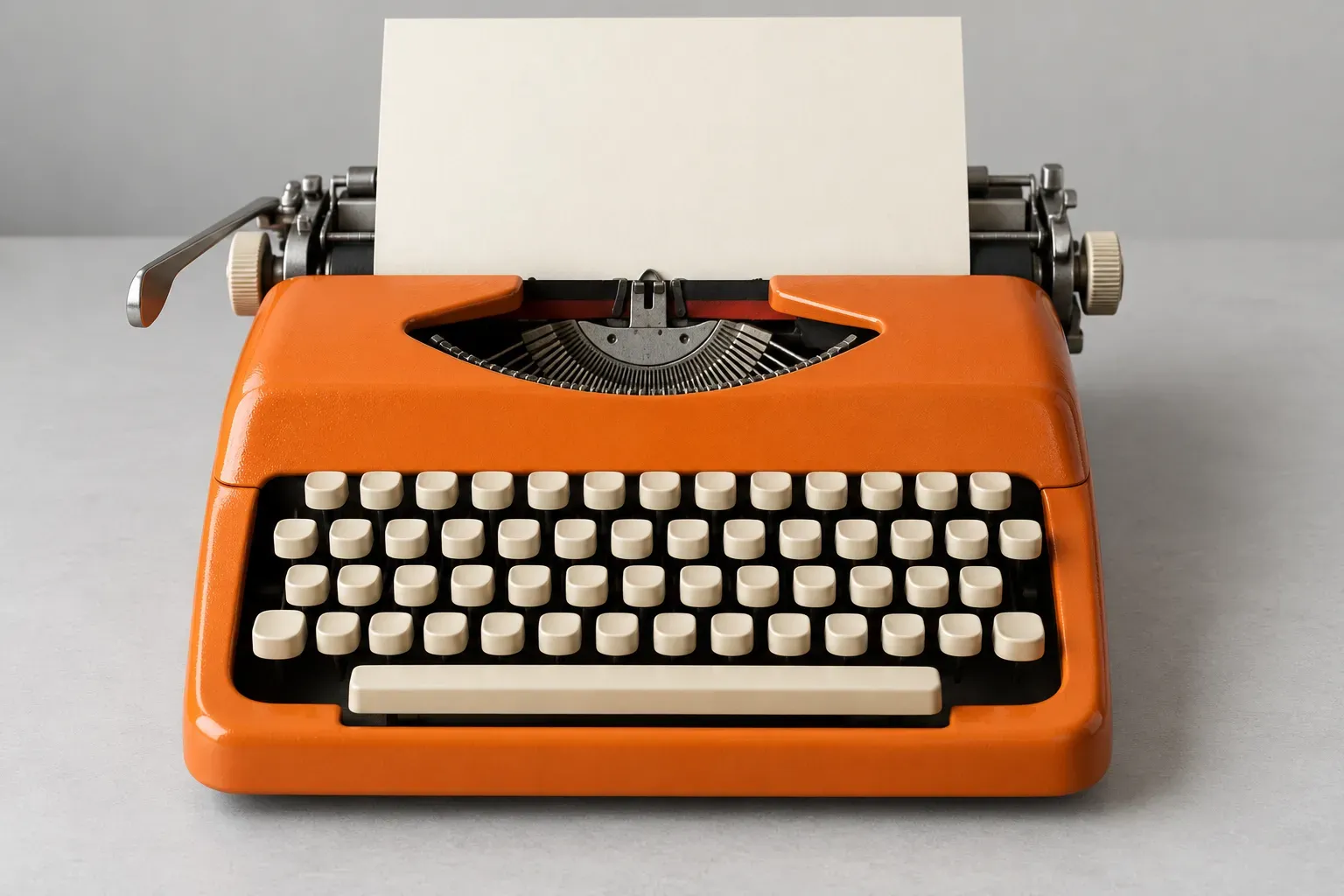 An orange typewriter with cream keys holds a blank sheet on a grey desk.